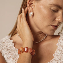 Close-up of woman wearing baroque pearl earrings, pearl necklace, orange gemstone bracelet, and lace top