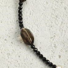 Close-up of black faceted beaded necklace with large brown agate bead on textured gray surface