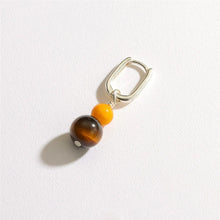 Silver earring with a yellow bead and a larger brown tiger's eye bead on a white background