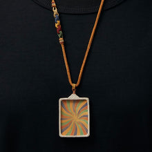 Tibetan-inspired pendant necklace with colorful swirl pattern on brown cord against black shirt