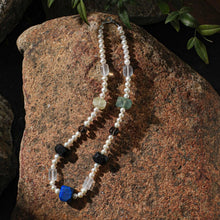 Pearl necklace with multicolored gemstone beads displayed on a rustic brown rock