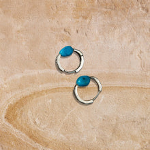 Silver hoop earrings with blue turquoise stones on textured beige stone surface