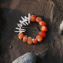 Agate gemstone and white pearl bracelet on dark sandy ground with stones