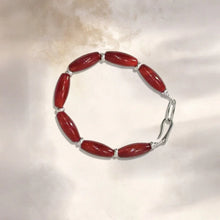 Red elongated bead bracelet with silver spacers and clasp on a light surface