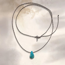 Brown cord necklace with blue teardrop pendant against light textured background