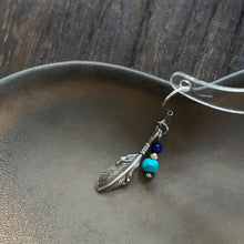 Silver feather charm earring with blue and turquoise beads on gray ceramic dish