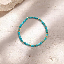 Turquoise and gold beaded bracelet on light textured stone surface with natural shadows