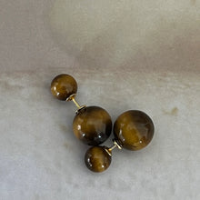Pair of double-sided tiger eye stone stud earrings with gold-tone posts on gray background