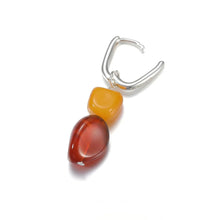 Silver hoop earring with two amber-like polished stones, one yellow and one reddish-brown, on white background