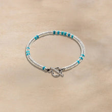 Silver beaded bracelet with turquoise accents and toggle clasp on beige background