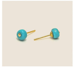 Close-up of gold stud earrings with round turquoise beads on neutral background
