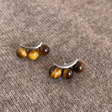 Silver crescent earrings with three polished tiger eye gemstone beads on brown fabric