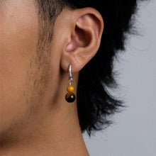 Close-up of a person's ear wearing a silver hoop earring with two brown and yellow beads
