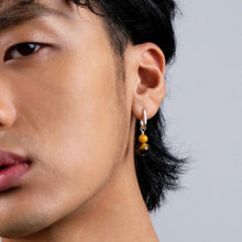 Close-up of young man wearing silver hoop earring with yellow and brown beads on gray background