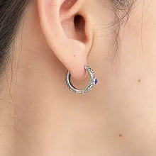 Close-up of ear wearing detailed silver hoop earring with blue gemstone