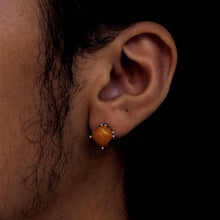 Close-up of ear wearing a square orange stud earring with silver prongs on dark skin