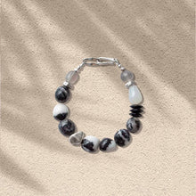 Handcrafted bracelet with black and white marbled stones and silver clasp on beige textured background