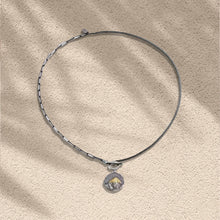 Silver necklace with textured round pendant featuring gold pyramid design on beige textured surface