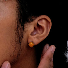 Close-up of ear with a yellow square stud earring held by hand against dark background