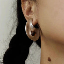 Close-up of a person's ear wearing a unique silver hoop earring with a central wooden detail