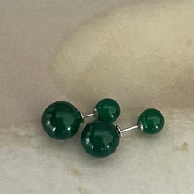 Pair of shiny green double spherical stud earrings on beige surface