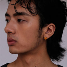 Close-up side profile of man wearing orange square stud earring with short black hair