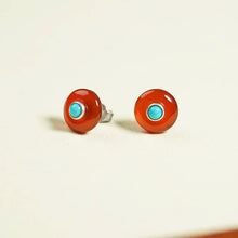 Round red stud earrings with turquoise center on white background