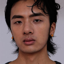 Close-up portrait of young Asian man with wet hair and orange stud earrings on gray background