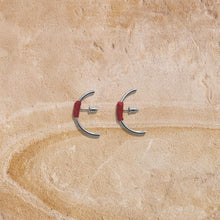 Pair of modern silver hoop earrings with red thread detail on textured beige surface