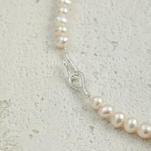 Close-up of irregular white pearl necklace with silver clasp on textured stone background