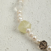 Close-up of a beaded bracelet with white pearls, a translucent yellow gemstone, and a smoky quartz bead on textured surface