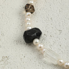 Close-up of a beaded necklace with white pearls, black and clear faceted stones on a textured surface