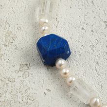 Close-up of blue gemstone, pearl beads, and clear crystal on textured stone surface