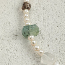 Close-up of pearl bracelet with green and transparent gemstones on textured surface