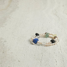 Elegant double-strand pearl bracelet with colorful gemstone beads on textured surface