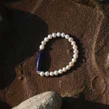 Pearl bracelet with a dark blue lapis lazuli bead on sandy beach among rocks