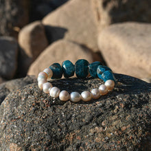 Blue stone and white pearl beaded bracelet on textured rock with blurred background stones