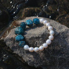 Bracelet with white pearls and blue rough stone beads on a gray rock by water