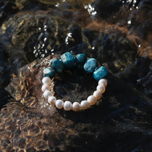 Blue stone and white pearl beaded bracelet on wet dark rock with water reflections