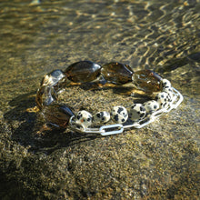 Smoky quartz and dalmatian jasper bead bracelets with silver chain on wet textured rock surface