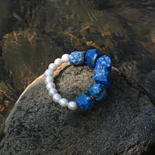 Pearl and blue gemstone beaded bracelet on textured rock by water surface