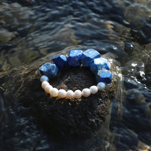 Blue gemstone and white pearl bracelet on wet rock surrounded by water
