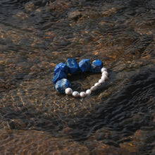 Beaded bracelet with blue stones and white pearls on wet river rock under clear water
