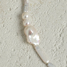 Close-up of an irregular white pearl necklace on textured light gray surface