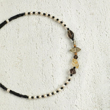 Delicate beaded necklace with black, white pearls and amber gemstones on textured white background