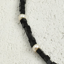 Black cube beads necklace with white pearl beads on textured light gray background