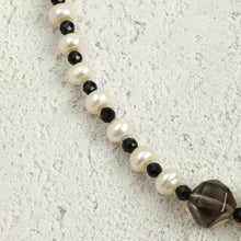 Close-up of pearl and faceted black bead necklace on textured light surface