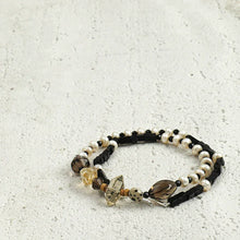 Double-strand beaded bracelet with black, white pearl, and amber-toned beads on textured white surface