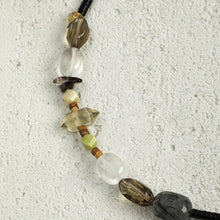 Close-up of a beaded necklace with assorted polished stones in black, green, and clear on textured white surface