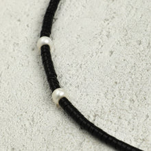 Close-up of black heishi beads necklace with white pearls on textured gray surface
